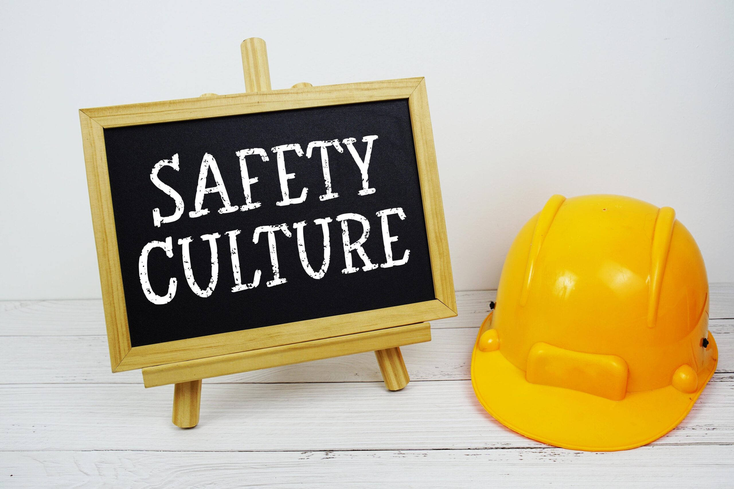 Safety Culture text on blackboard with safety helmet on wooden background