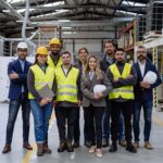 Full team of warehouse employees standing in warehouse. Team of workers, managers and female director in modern industrial factory, heavy industry, manufacturer. Group portrait.